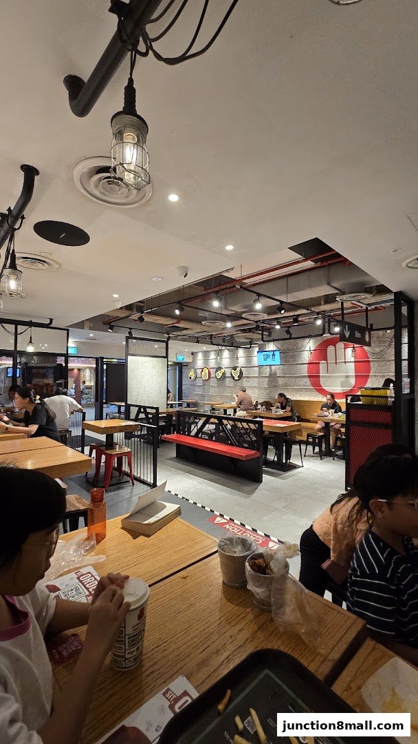 Interior view of a busy 4 Fingers Crispy Chicken restaurant with diners and industrial-style decor.