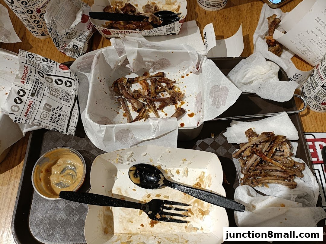 A messy table after eating crispy chicken, with leftover bones, wrappers, and a dipping sauce.