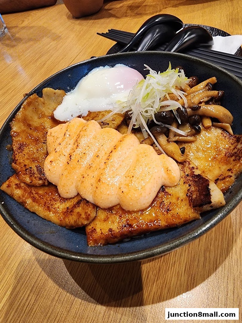 A close-up of a Japanese rice bowl with grilled pork, a poached egg, and mushrooms.