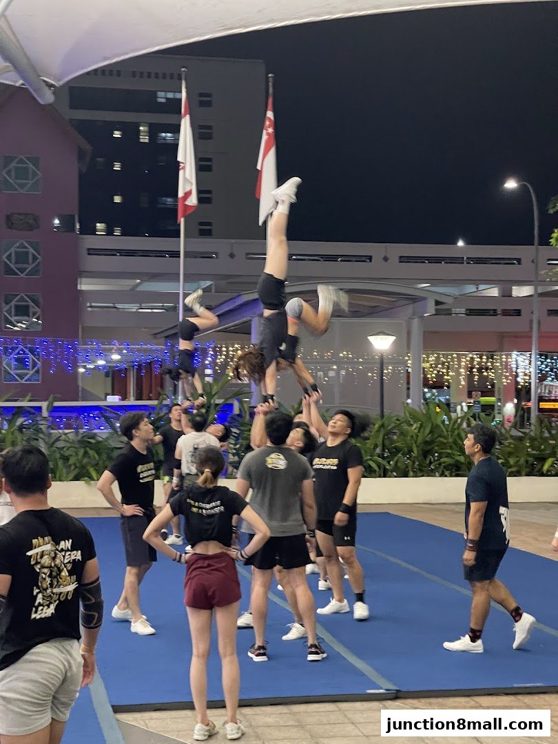 A group of people practicing a cheerleading stunt on a blue mat outdoors at night.