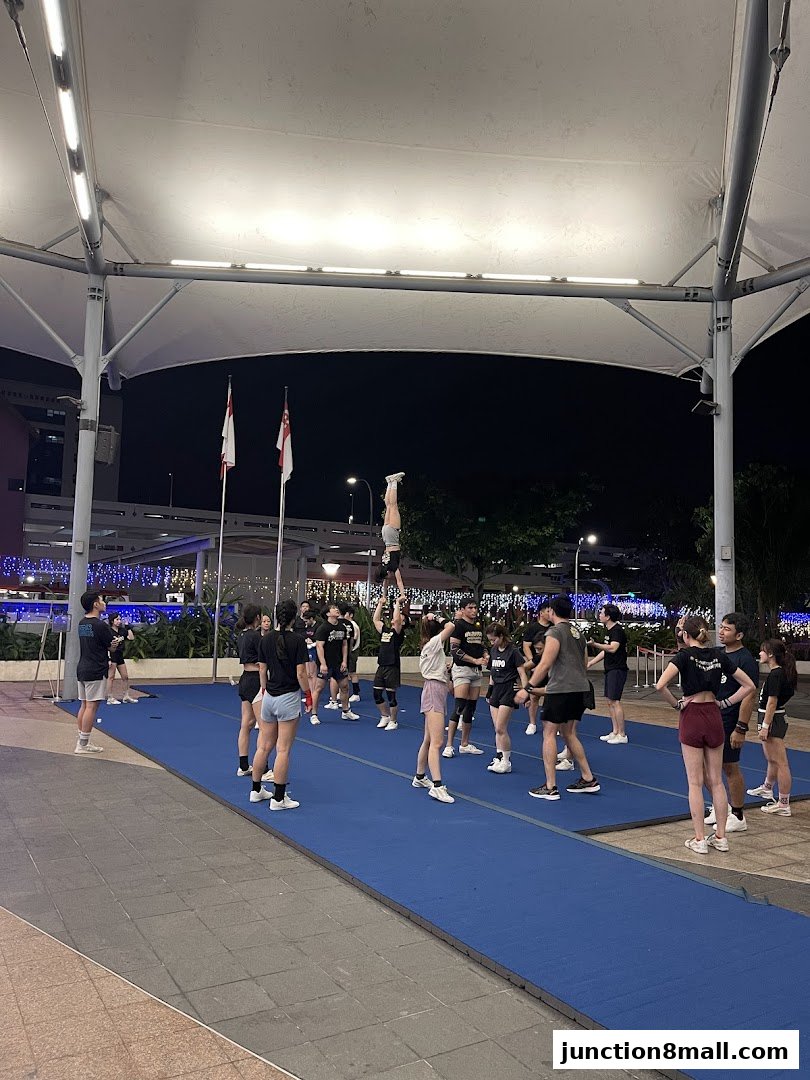 A group of people practicing cheerleading stunts on a blue mat outdoors at night.