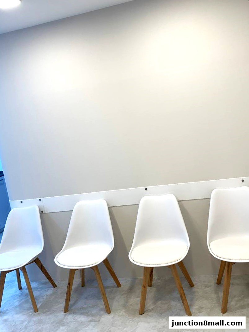 A waiting area with four white chairs with wooden legs against a light-colored wall.