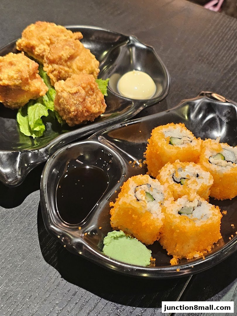 A close-up of Japanese fried chicken and California rolls served with dipping sauce and wasabi.