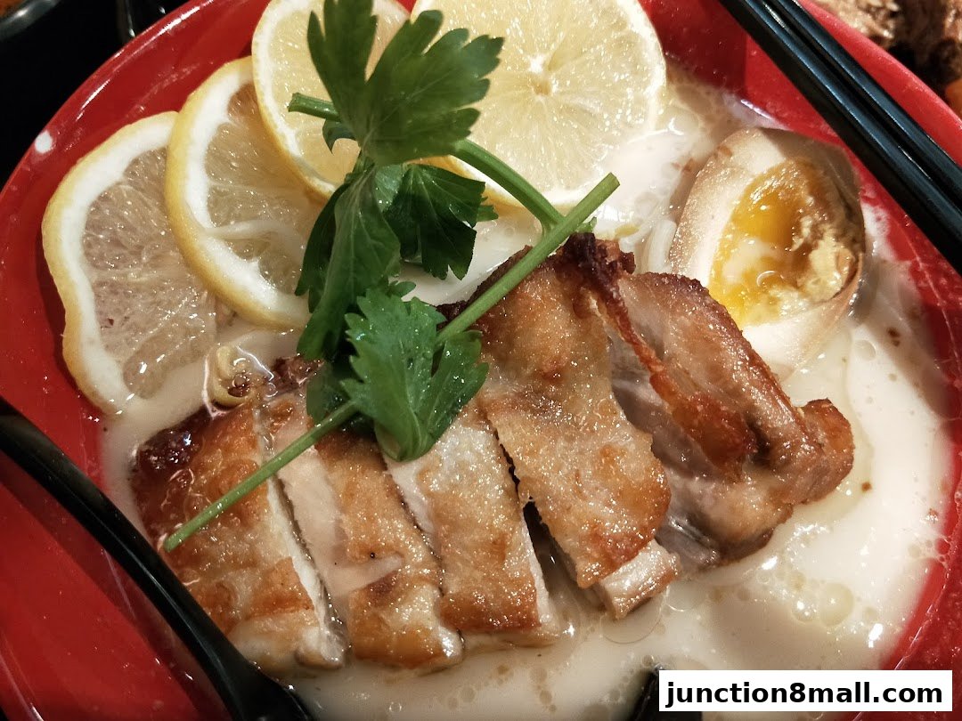 A close-up of a bowl of Ajisen Ramen with sliced chicken, a soft-boiled egg, and lemon slices.