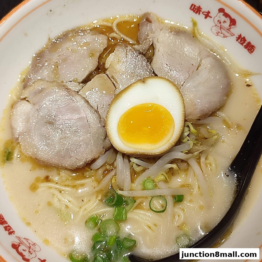 A bowl of Ajisen Ramen with tender pork slices, a soft-boiled egg, and bean sprouts.