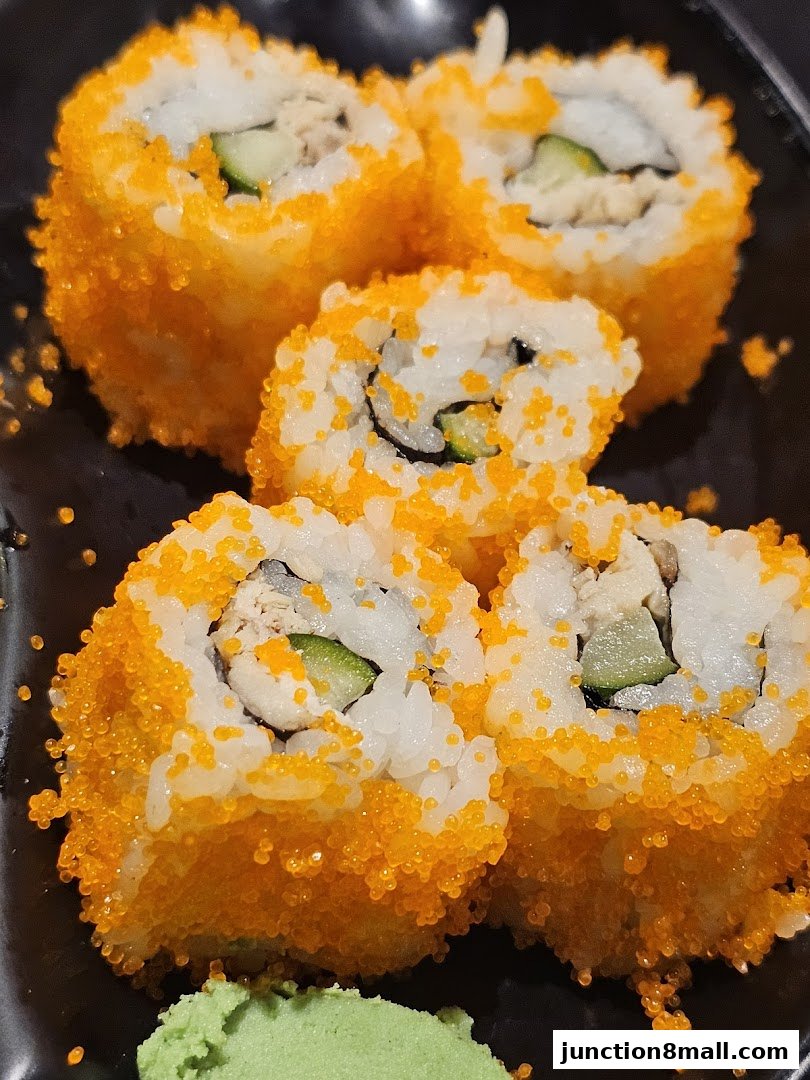 A close-up shot of California rolls covered in bright orange tobiko with a side of wasabi.