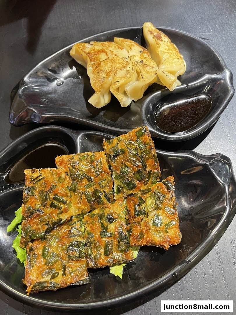 Two black plates with Japanese food: pan-fried dumplings and savory chive pancakes with dipping sauce.