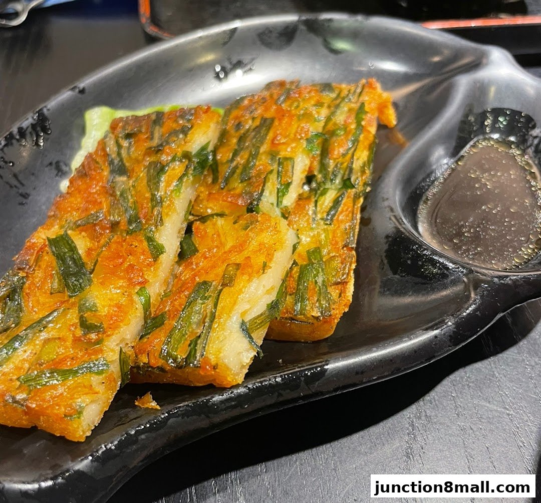 A close-up of a savory pan-fried dish with chives and a dipping sauce.