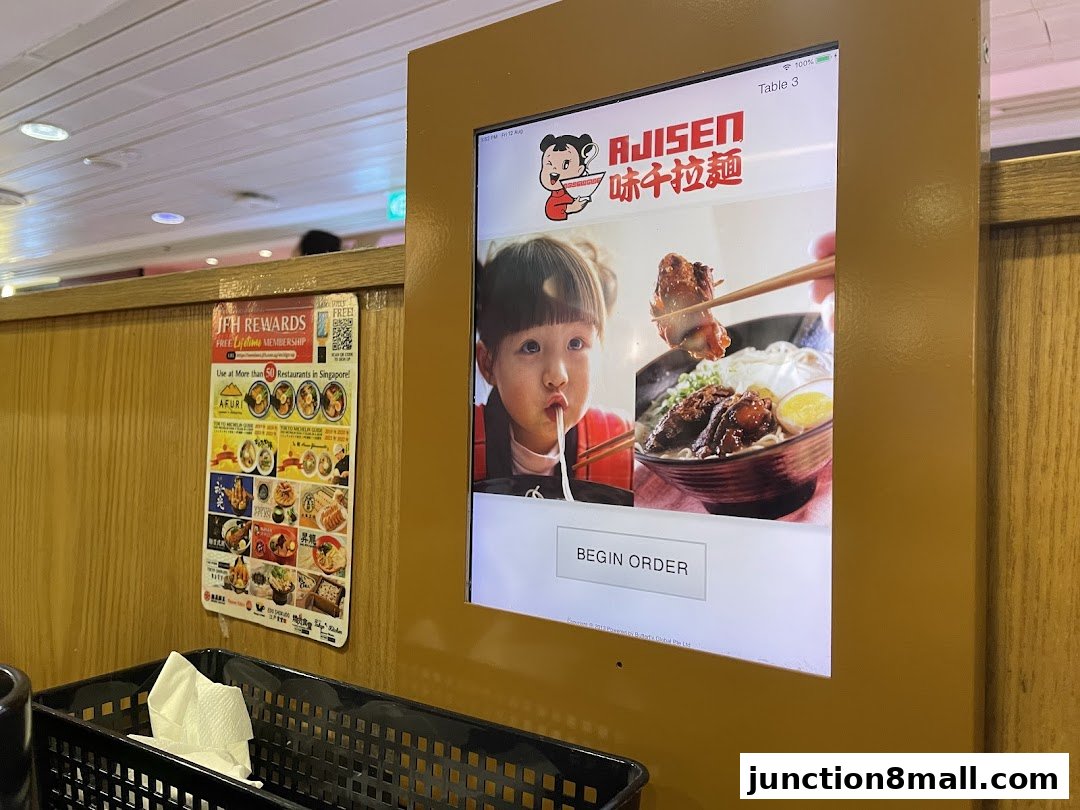 An Ajisen Ramen ordering kiosk with a promotional poster on the side.