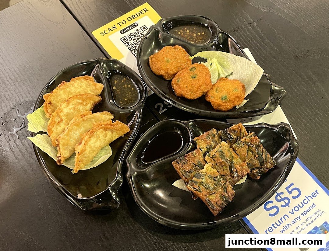 Three black plates of assorted fried appetizers and dipping sauce on a black table.