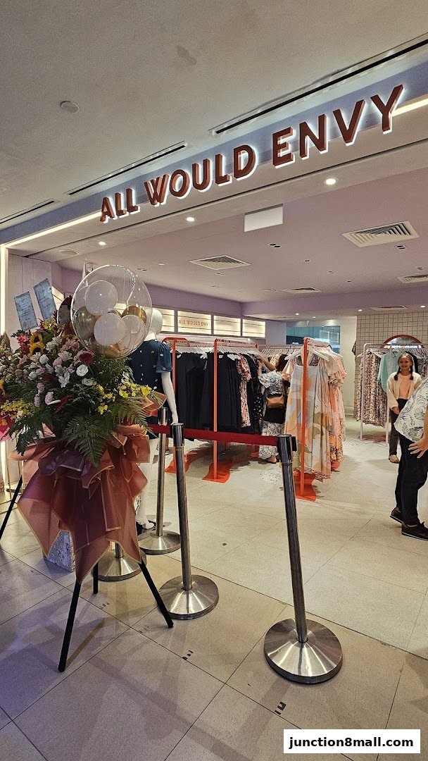 The entrance of a clothing store with a floral display and racks of dresses.