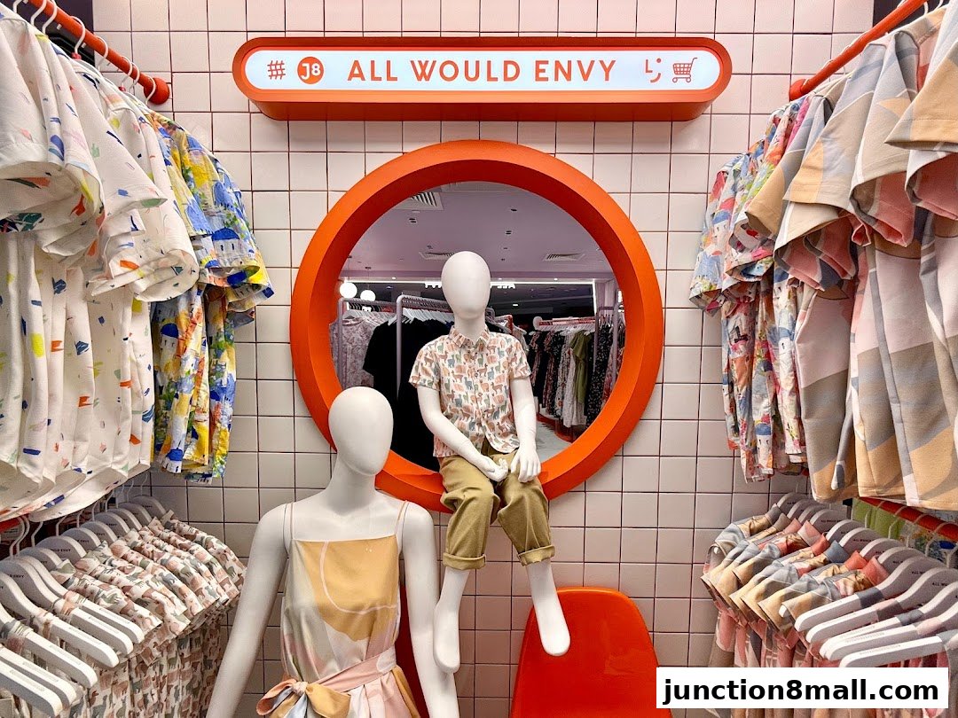Mannequins display colorful patterned shirts and dresses in a brightly lit clothing store.