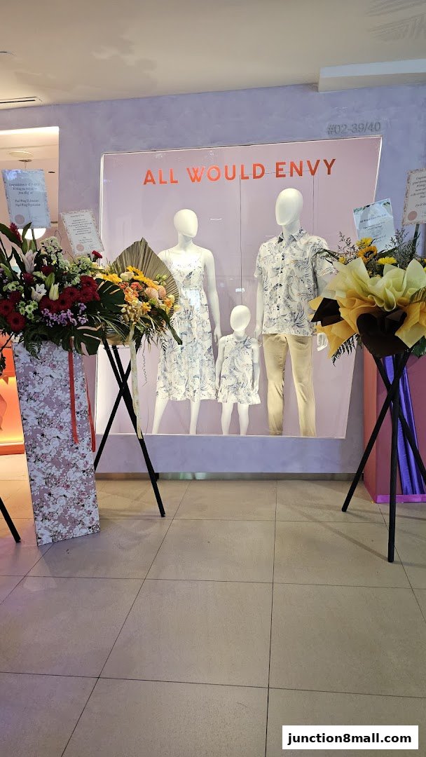 Mannequins display matching family outfits in a shop window with floral arrangements.