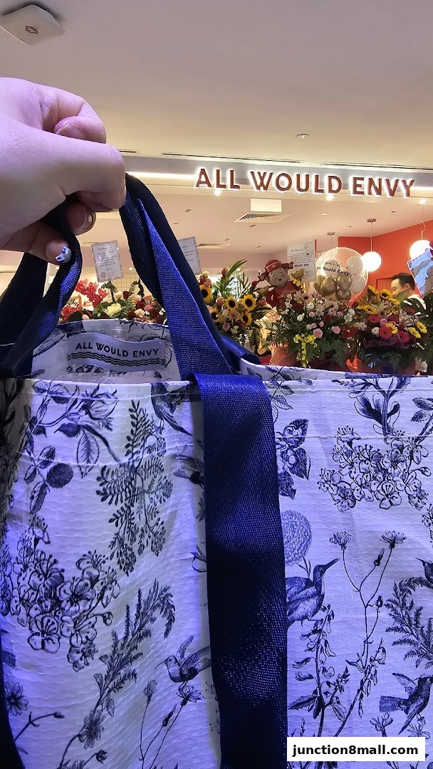 A person holds a patterned bag in front of the "ALL WOULD ENVY" shop entrance.