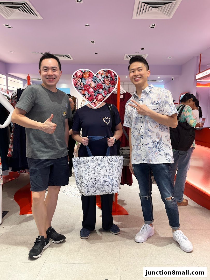 Three people posing in a clothing store, one holding a patterned tote bag.