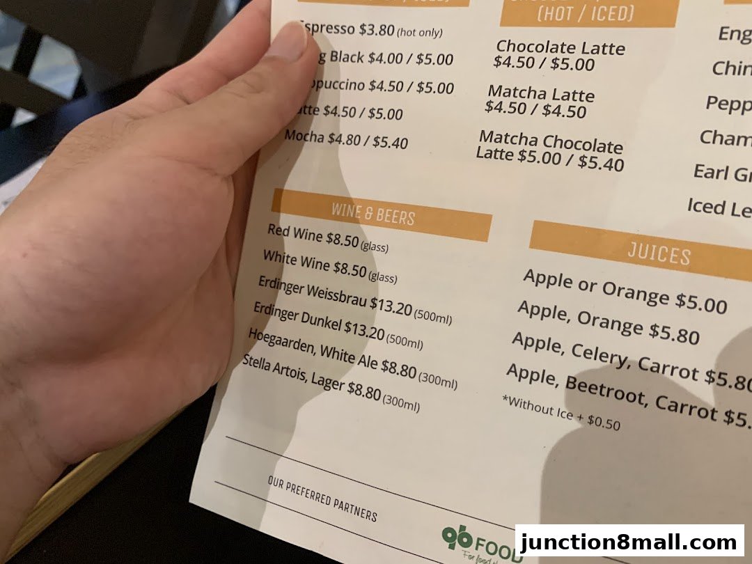 A hand holds a menu with various drinks and beverages, including coffee, wine, beer, and juices.
