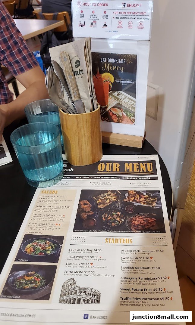 A table setting at Ambush restaurant with menus, cutlery, and drinks.