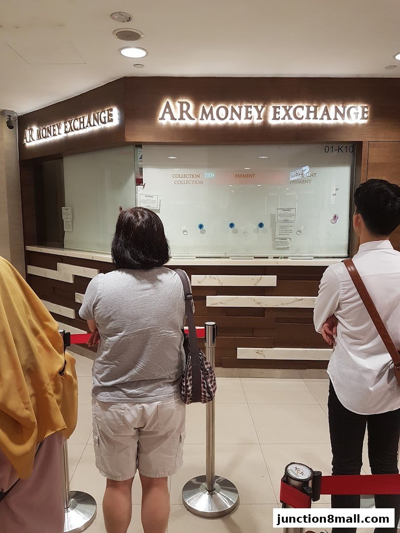 People queue at the AR Money Exchange counter with illuminated signage.