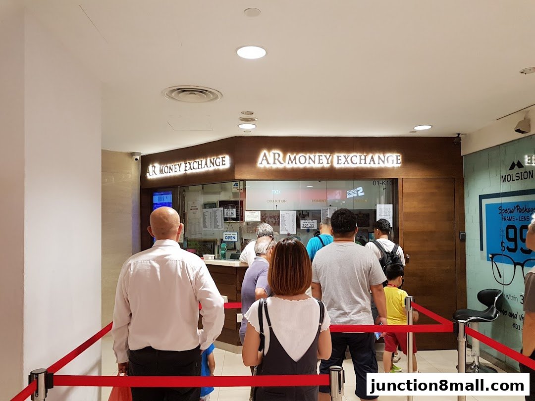 People queue at AR Money Exchange, a shop with a prominent sign and display.