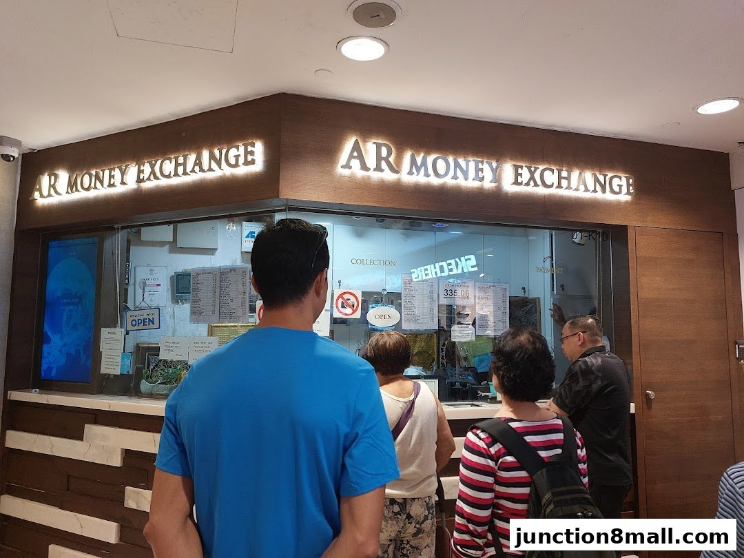 People queuing at AR Money Exchange counter with exchange rates displayed.