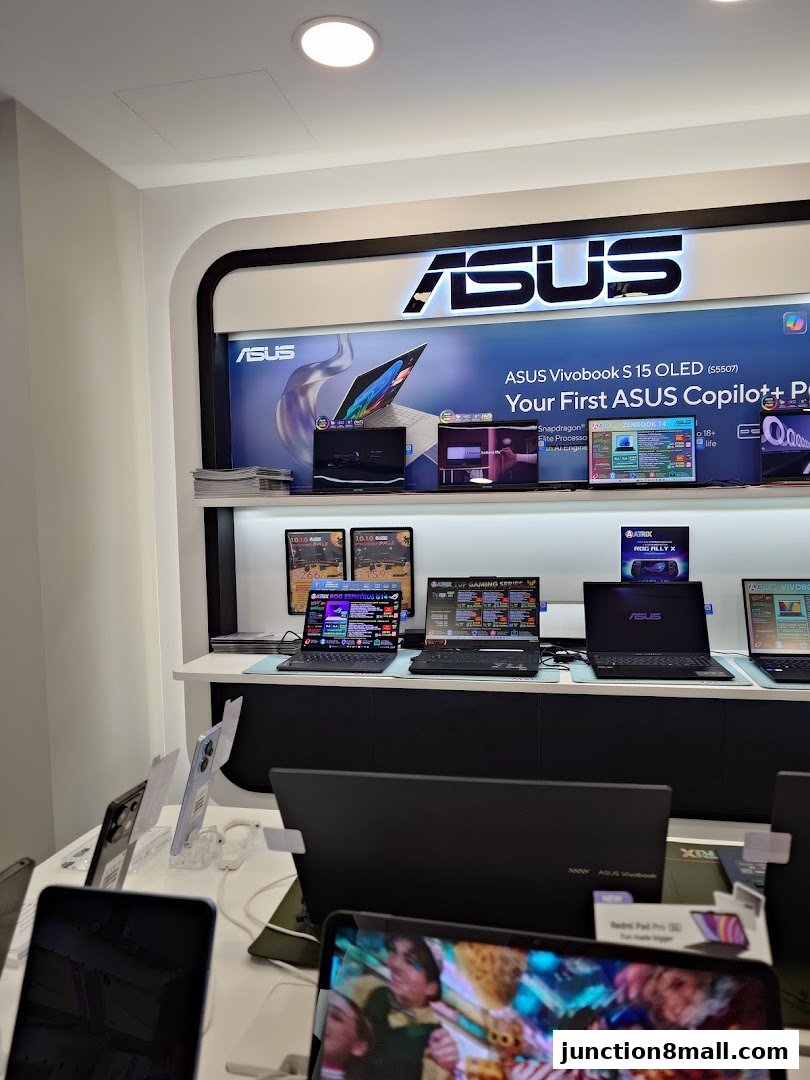 An ASUS store display featuring laptops, monitors, and phones, with prominent branding.