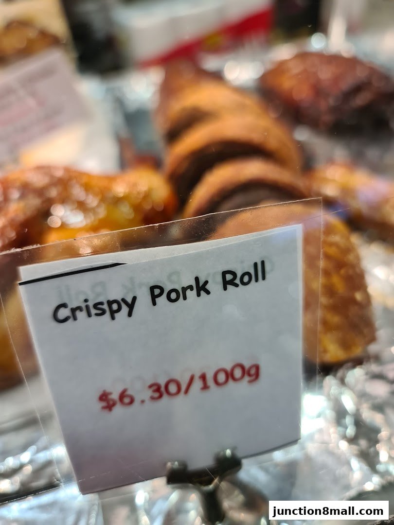 A close-up of a sign for 'Crispy Pork Roll' with a price of $6.30/100g.