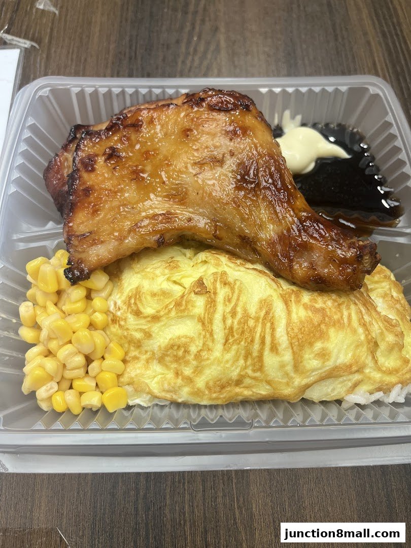A delicious BBQ chicken leg with omelet, rice, corn, and sauce in a takeout container.