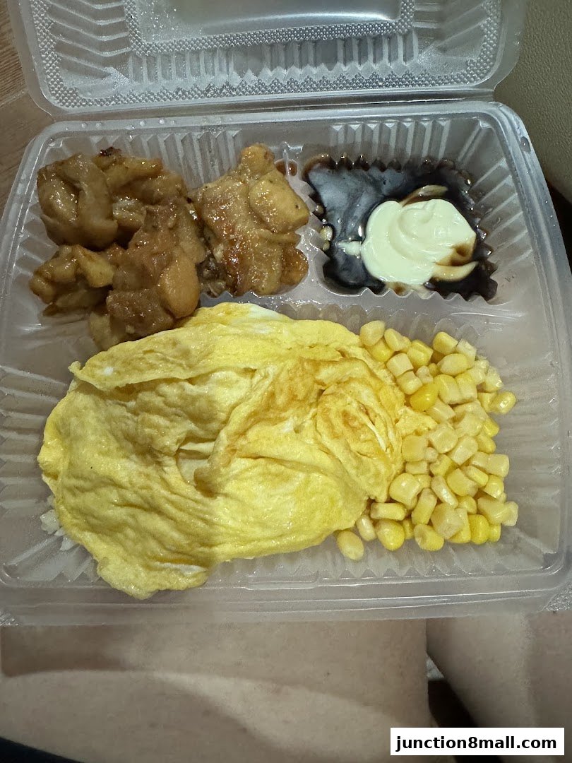 A takeout container filled with a meal including chicken, omelet, corn, and sauce.