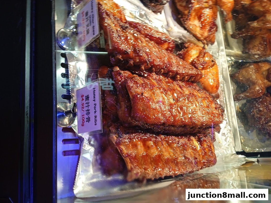 Close-up of glistening honey pork ribs and roasted chicken pieces in a display case.