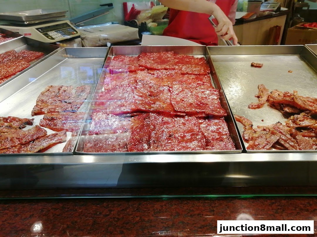 A display of various types of bak kwa (dried meat) in metal trays at a food stall.