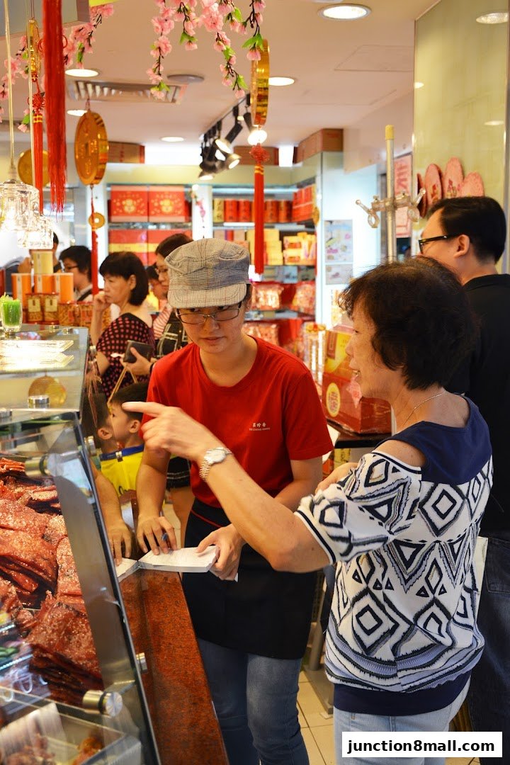 A shop assistant serves a customer at a counter displaying meat products.
