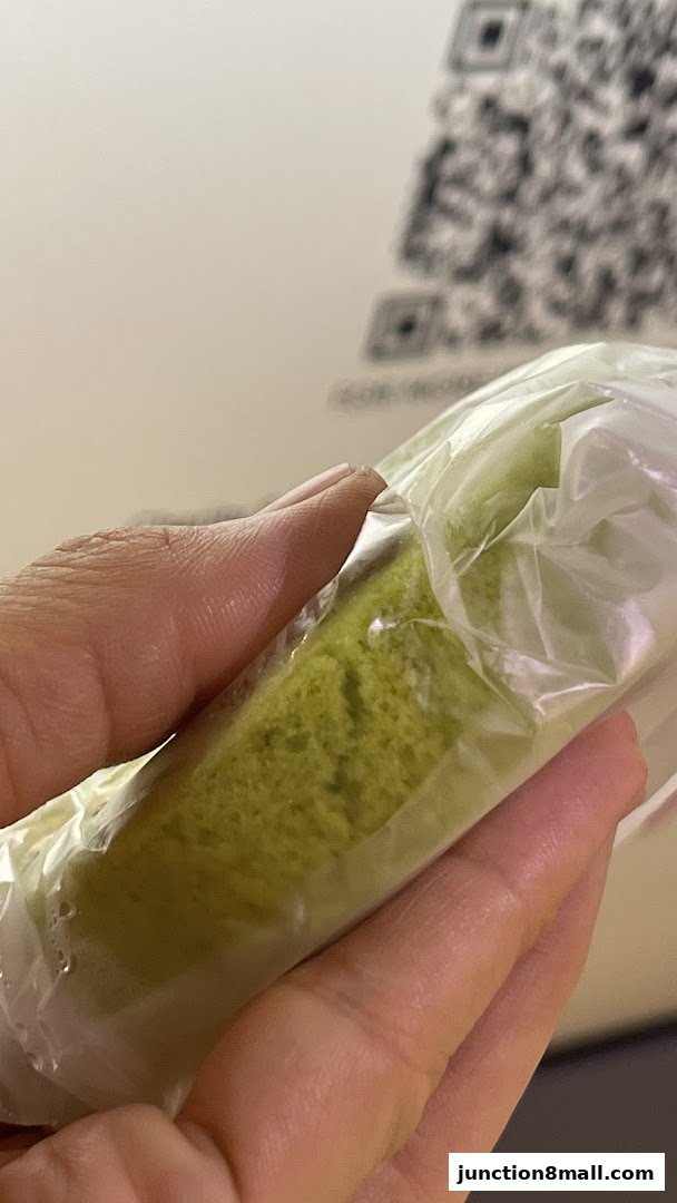 A hand holds a wrapped green cake slice with a QR code in the background.