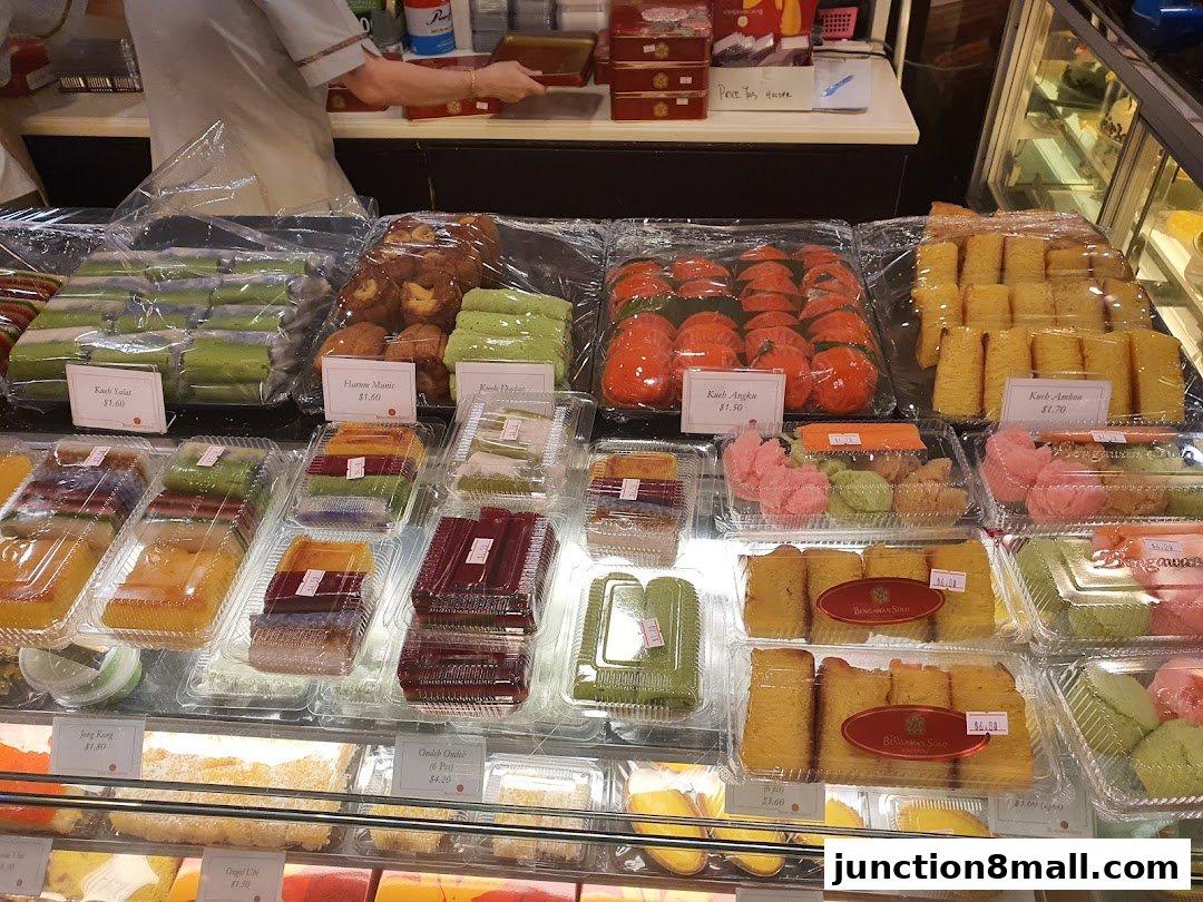 A display of various colorful traditional cakes and pastries in clear plastic packaging.