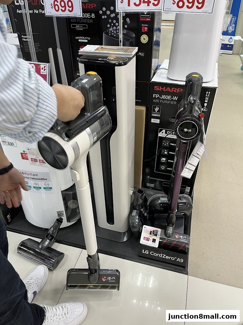 A person is examining LG CordZero vacuum cleaners and Sharp air purifiers on display.