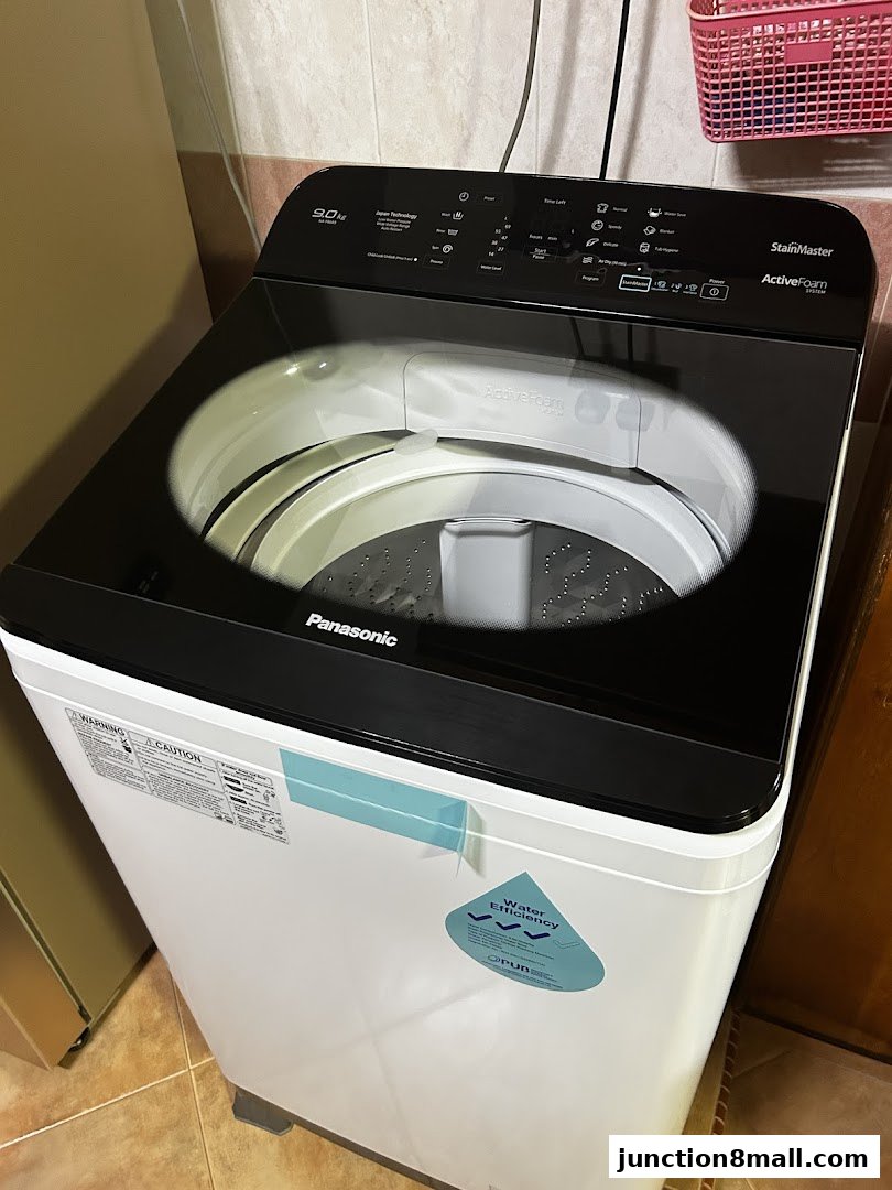 A top-loading Panasonic washing machine with a black glass lid and control panel.