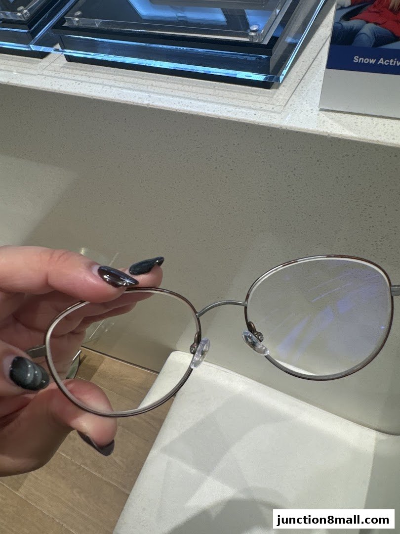 A hand holds a pair of stylish, round-framed eyeglasses with clear lenses.