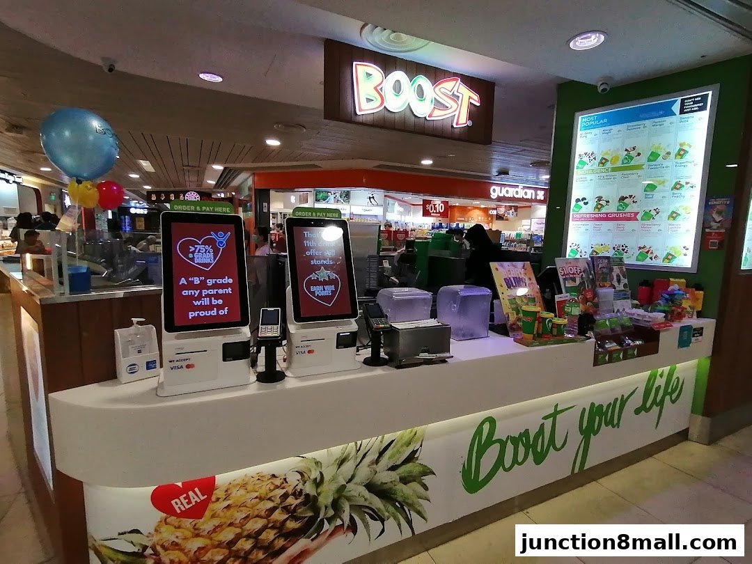 The Boost Juice shop counter with ordering kiosks, a menu board, and promotional balloons.