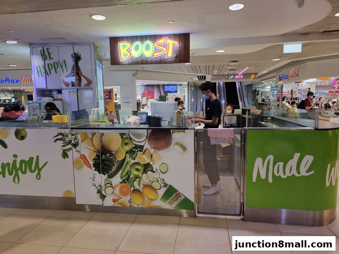 A Boost Juice shop counter with staff preparing drinks and vibrant fruit graphics.