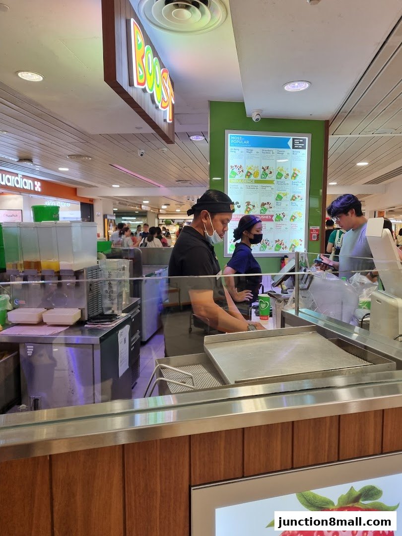 Staff members are preparing drinks behind the counter at Boost Juice, with a menu board visible.