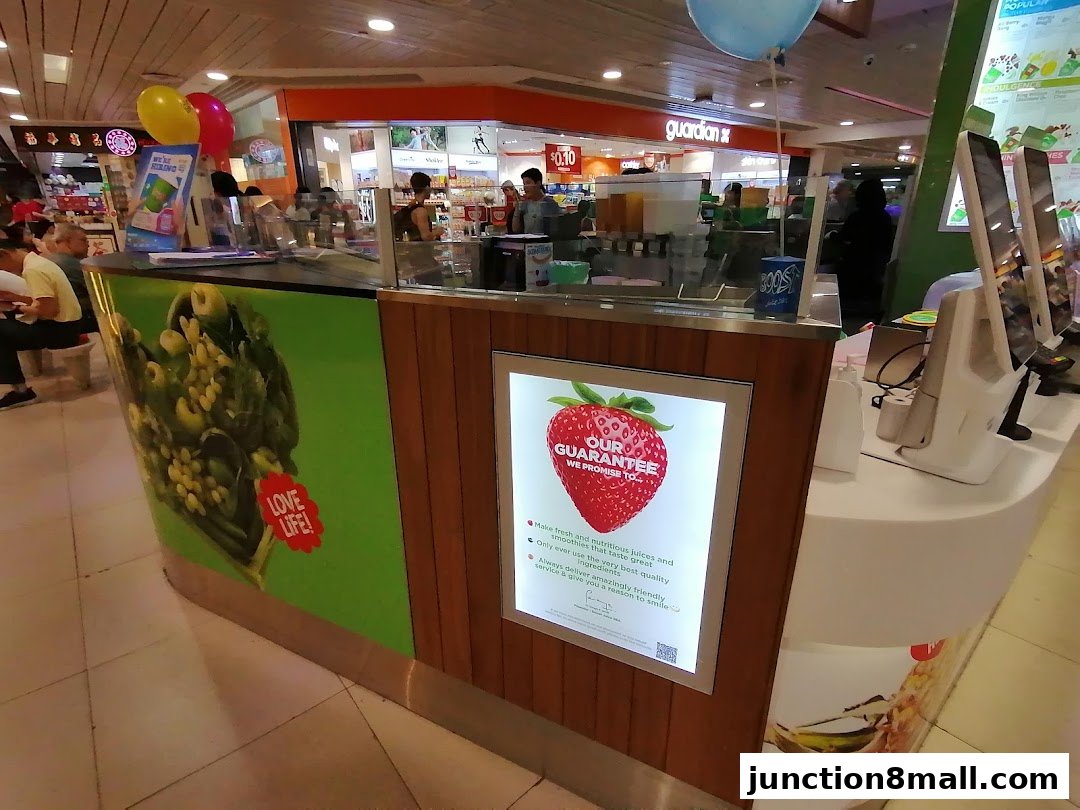 A Boost Juice counter with colorful branding, a strawberry guarantee sign, and digital ordering screens.
