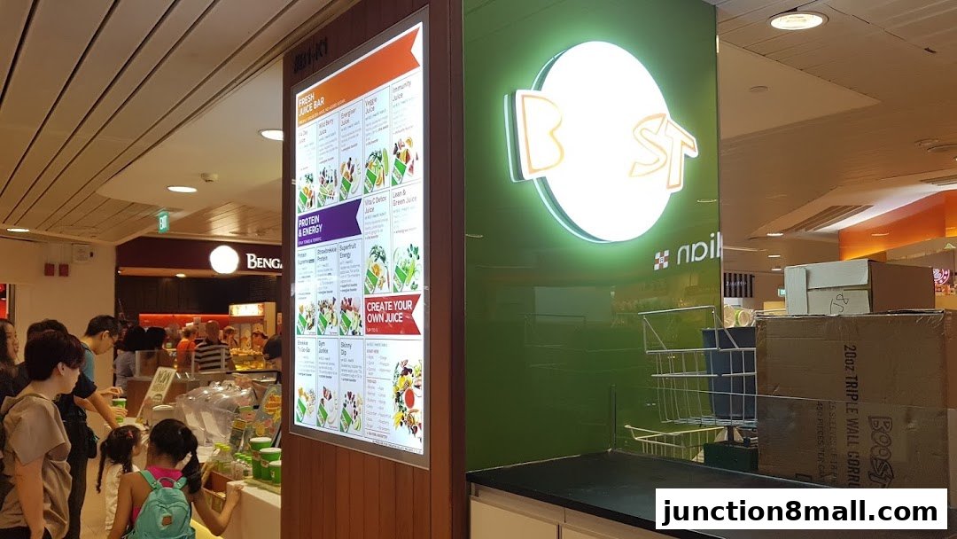 A Boost Juice shop with a bright menu board and neon logo, showing customers queuing.