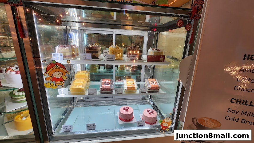 A display case filled with various cakes and pastries, with a menu board visible on the right.