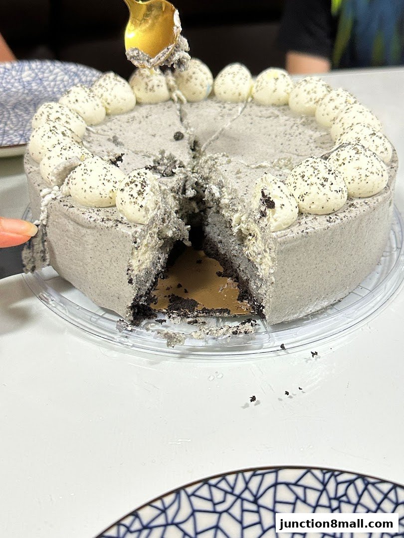 A slice is being taken from a grey cake with white frosting and black sprinkles.