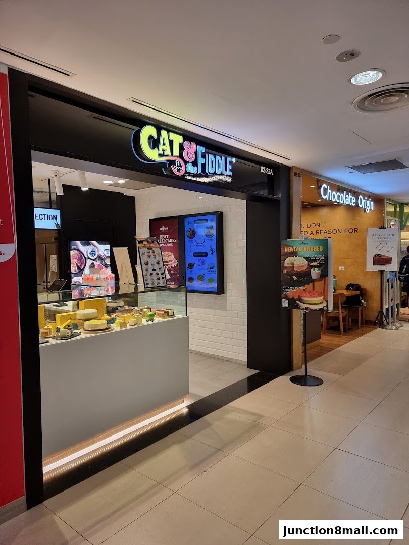 The exterior of a dessert shop called Cat & the Fiddle, showcasing cakes and a menu display.