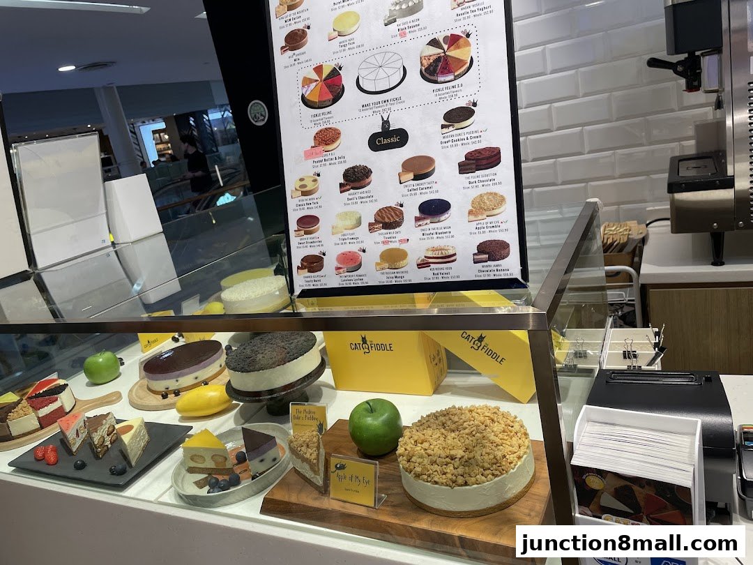 A display case filled with various cakes and a menu board from Cat the Fiddle Cakes.