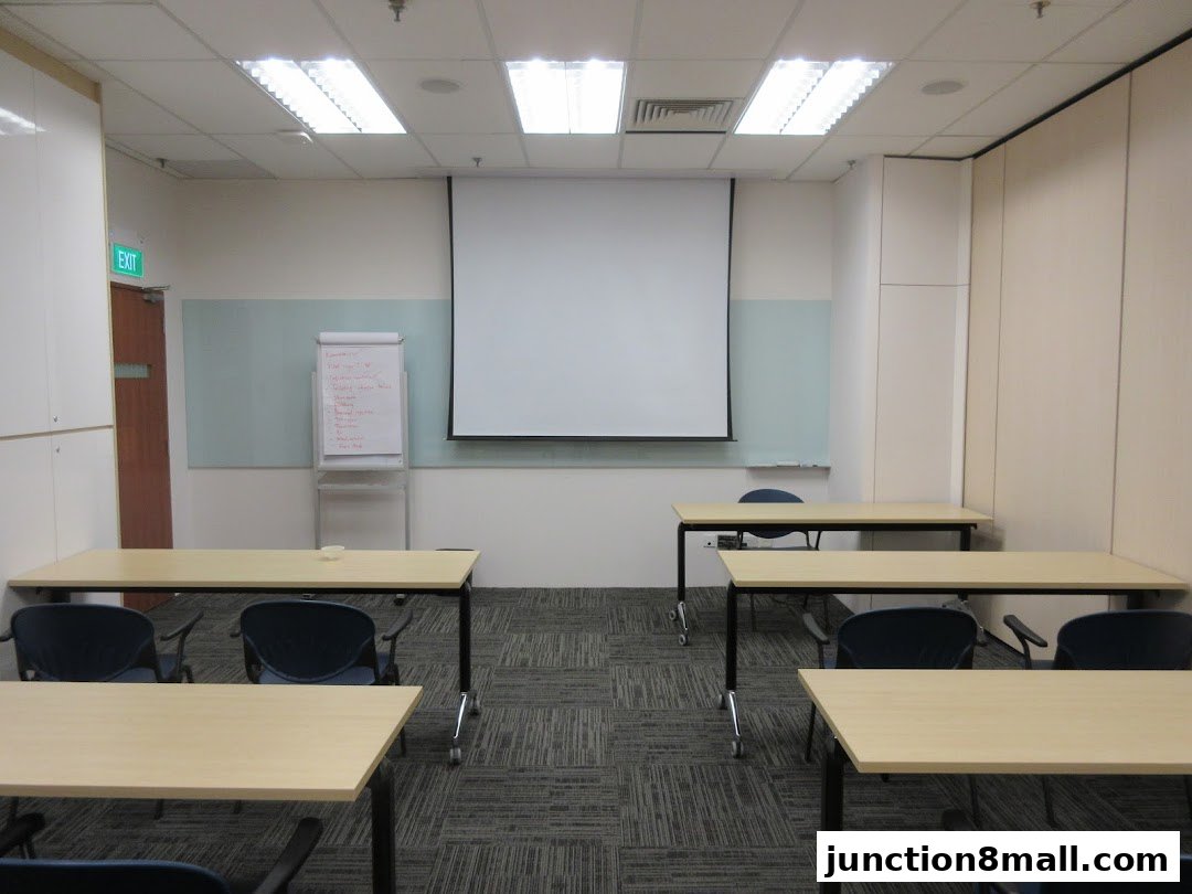 A classroom or meeting room with tables, chairs, a whiteboard, and a projector screen.