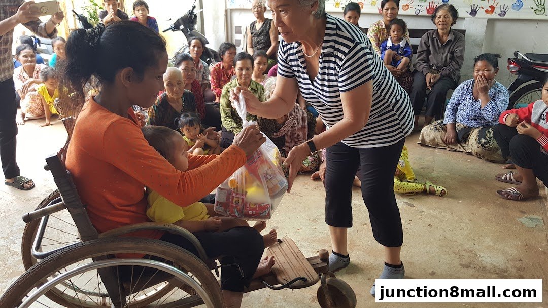 A woman in a wheelchair receives a bag of groceries from another woman, with a group of people watching.