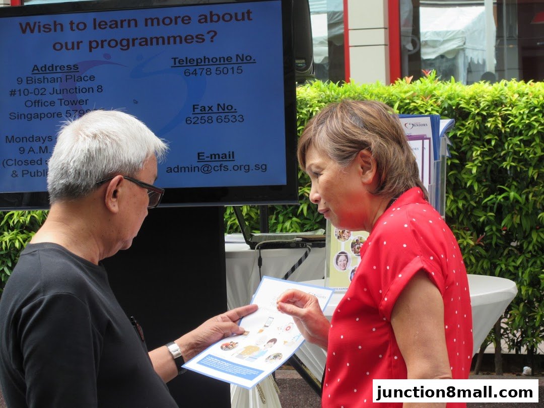 Two people are looking at a brochure in front of a screen displaying program information.