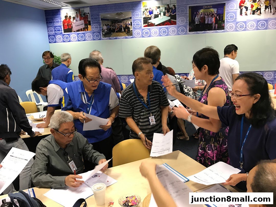 A group of seniors are gathered around tables, looking at papers and interacting.