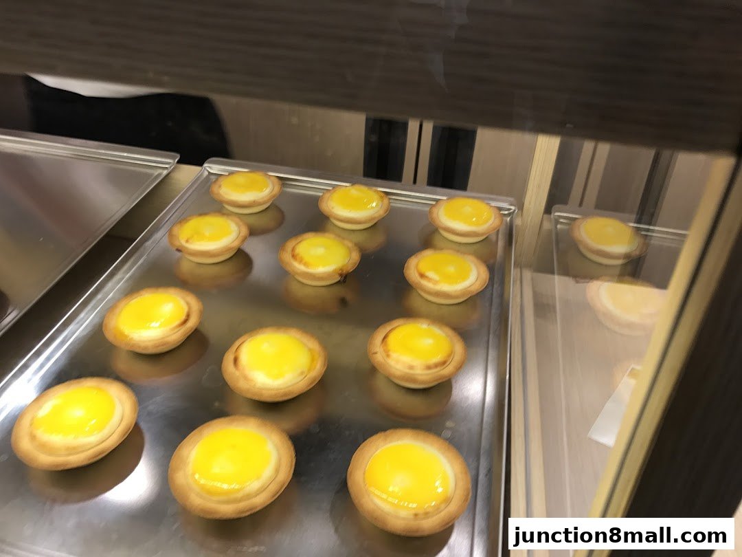 A display of freshly baked egg tarts on metal trays inside a shop.